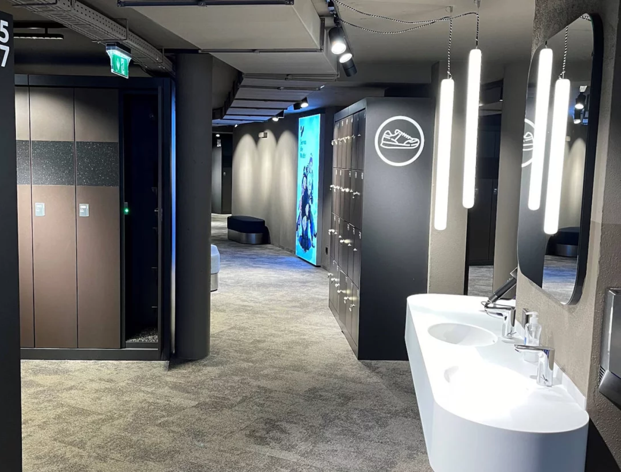 Moderne, elegante Toiletten mit schlanken weißen Waschbecken, großen Spiegeln und gepolsterten Sitzgelegenheiten. Sanfte Beleuchtung und Kunstwerke unterstreichen das raffinierte Ambiente.