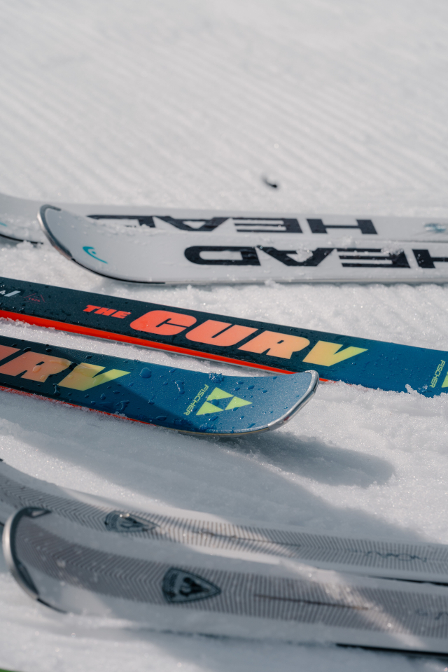 Vier bunte Skier liegen auf einem schneebedeckten Hang. Die Skier sind mit Logos und Markenzeichen versehen, die einen sportlichen und abenteuerlichen Eindruck vermitteln.