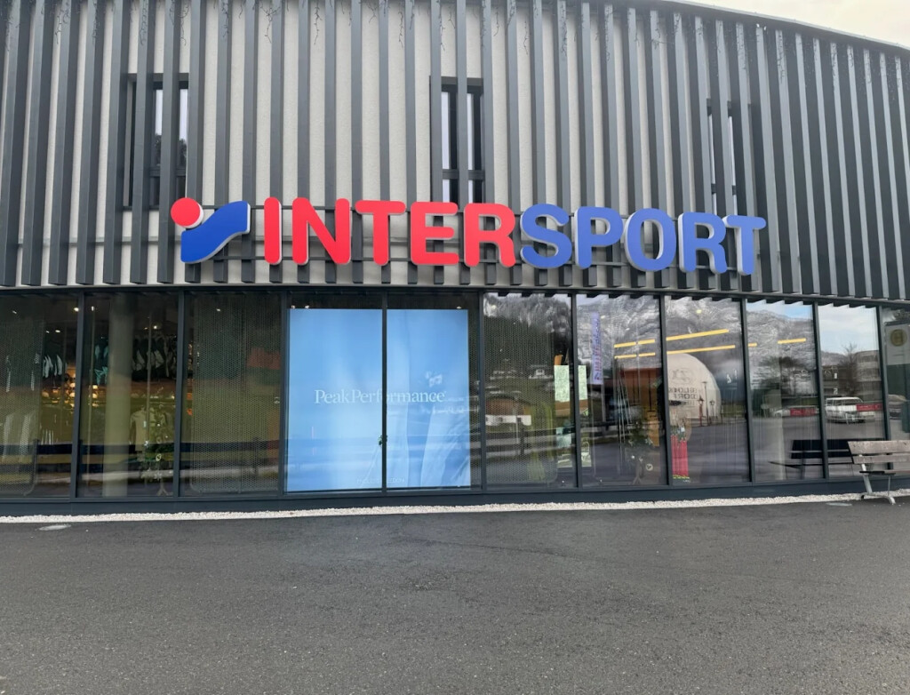Exterior view of an Intersport store with a modern façade, large glass windows, and a clearly visible logo. The atmosphere is calm and inviting.