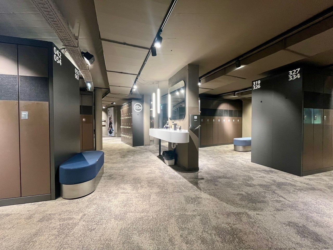 Moderne Umkleidekabine mit grauem Teppich, Schließfächern, Waschbecken und Sitzbank.