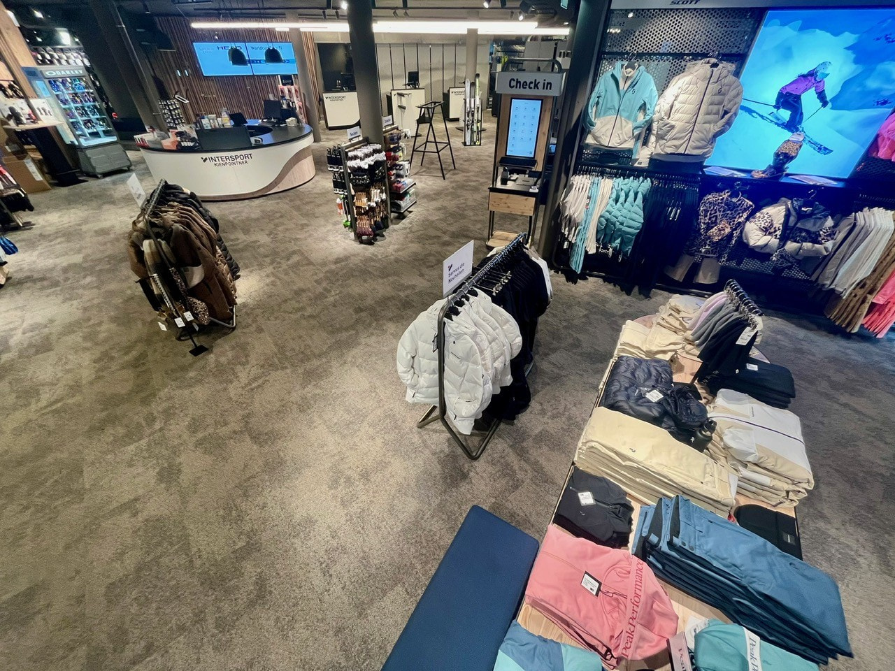 Clothing store interior with racks of apparel, folded jeans, jackets, and a checkout counter.