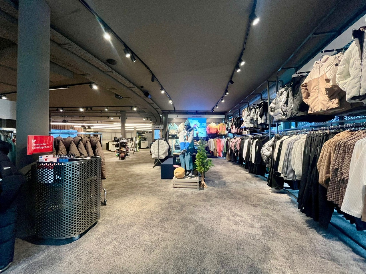 Clothing store interior with racks of apparel, jackets, and sweaters for sale. Retail fashion shopping.