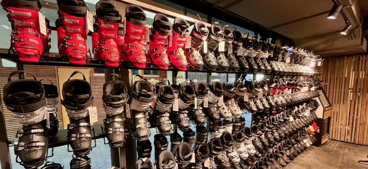 Ski shop display: Rows of red and black ski boots on shelves for sale or rental.