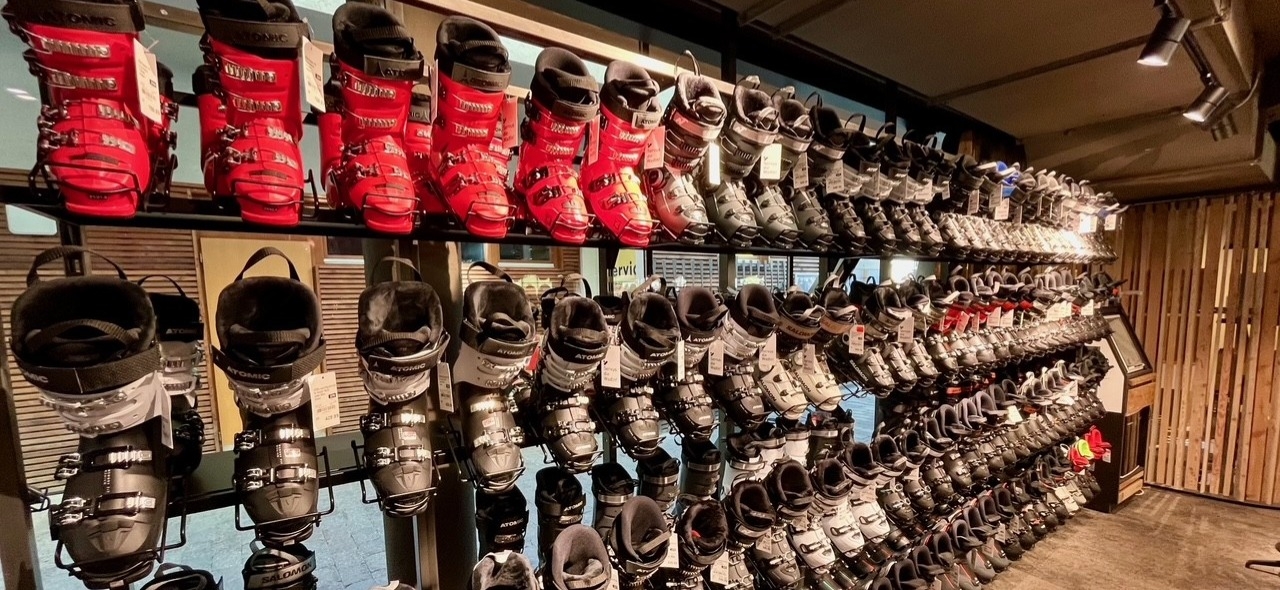 Auslage im Skigeschäft: Reihen von roten und schwarzen Skischuhen in Regalen zum Verkauf oder Verleih.