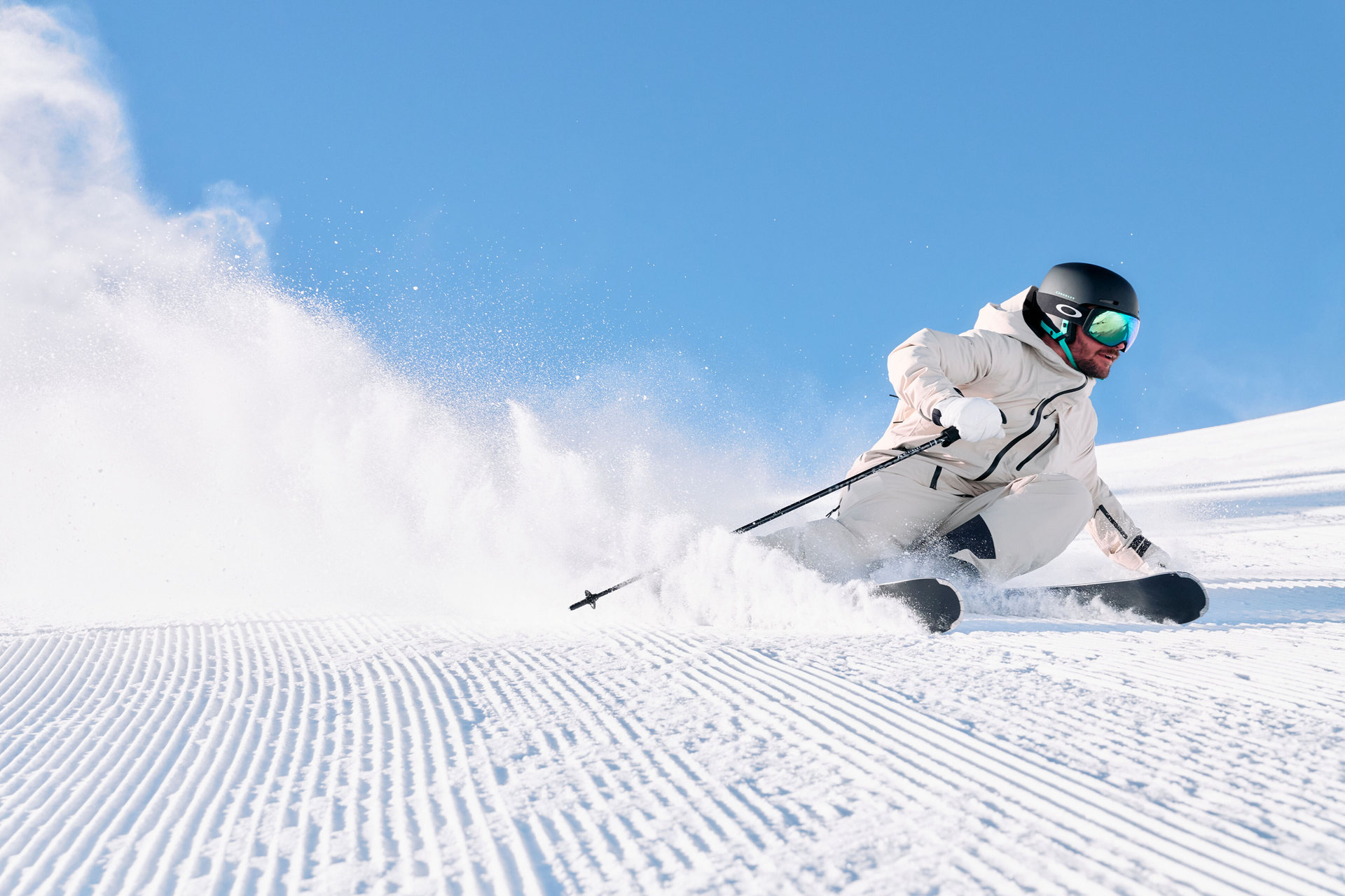 Skifahrer in weißer Ausrüstung carvt mit hoher Geschwindigkeit durch frischen Pulverschnee unter blauem Himmel.